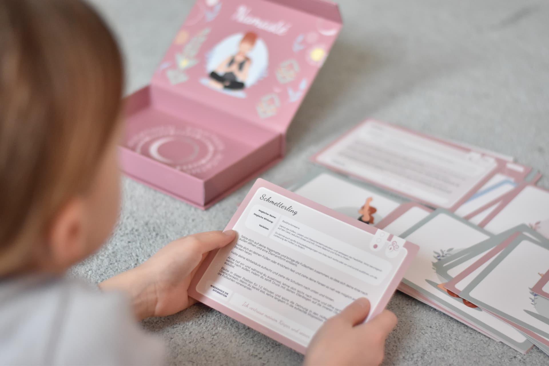 Mädchen liest die Yoga-Karte Schmetterling neben der Yomeda Kartenbox