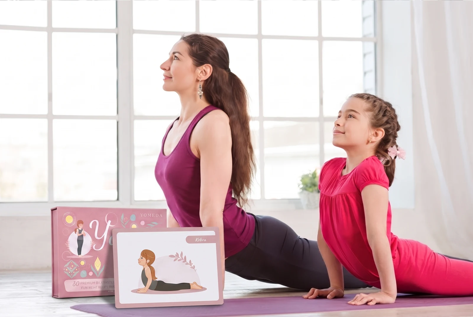 Mutter und Tochter üben gemeinsam die Kobra-Pose auf der Yogamatte, davor die Yomeda Yoga-Bildkarten Box mit der aufgestellten Kobra-Karte
